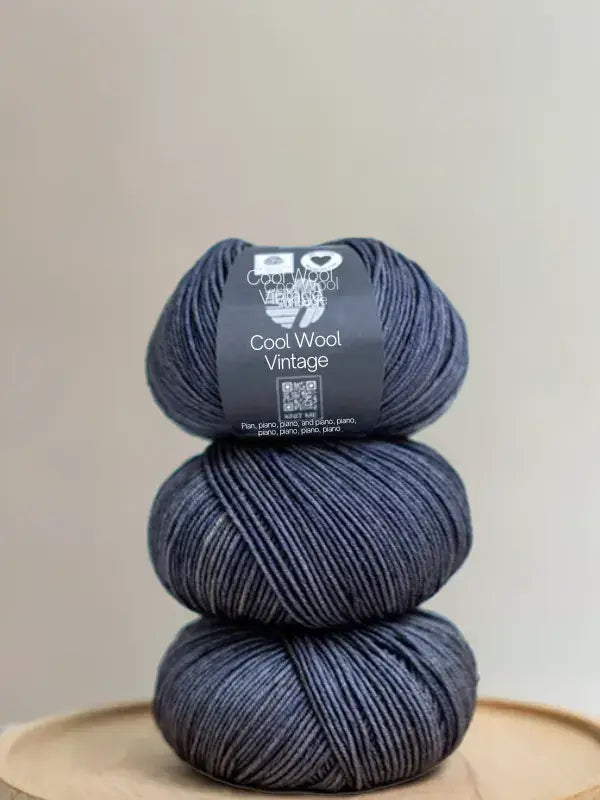Three stacked balls of dark grey Lana Grossa Cool wool vintage yarn with a product label on the top ball.