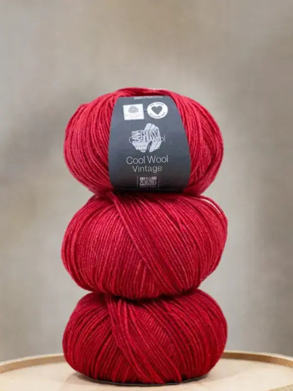 A stack of three balls of soft, bright red Lana Grossa Cool wool vintage yarn.