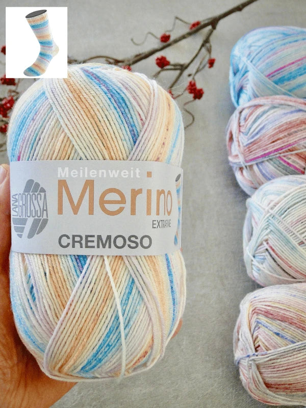 A hand holds a skein of pastel multicolored Lana Grossa Meilenweit 100 Merino Extrafine Cremoso yarn. Three more konepestävä merinovilla skeins rest on a gray surface with red berries in the background. A small sock image is top left.