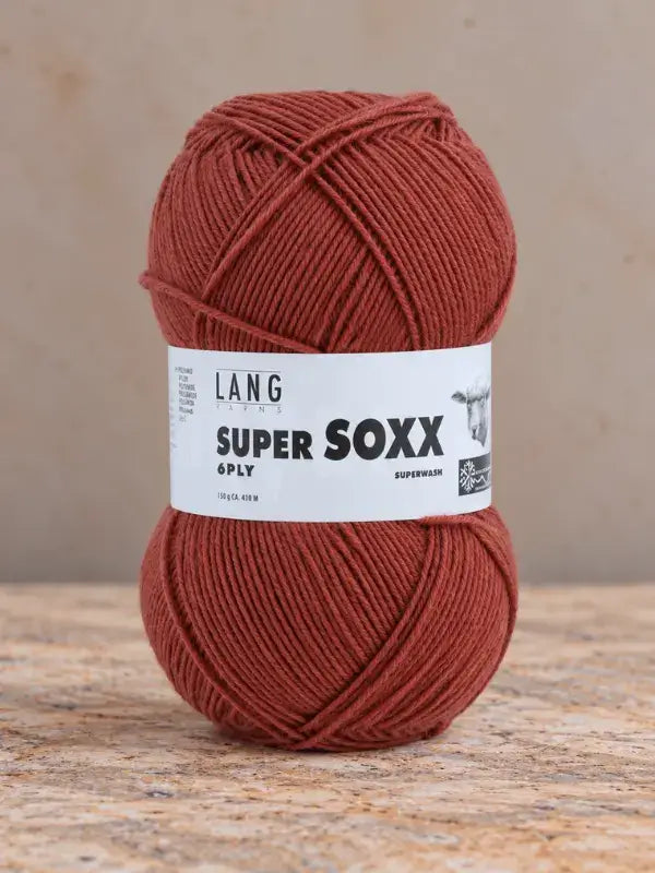 A ball of terracotta-colored Lang Yarns Super Soxx 6 ply – kestävä sukkalanka villasta yarn with a label.