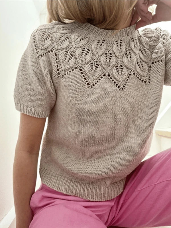 A person sits on stairs in a beige Le Knit Sommer Ella neuleohje, ENG top with an intricate lace yoke and bright pink pants, their face partially turned away from the camera, highlighting this stylish knitwear look.