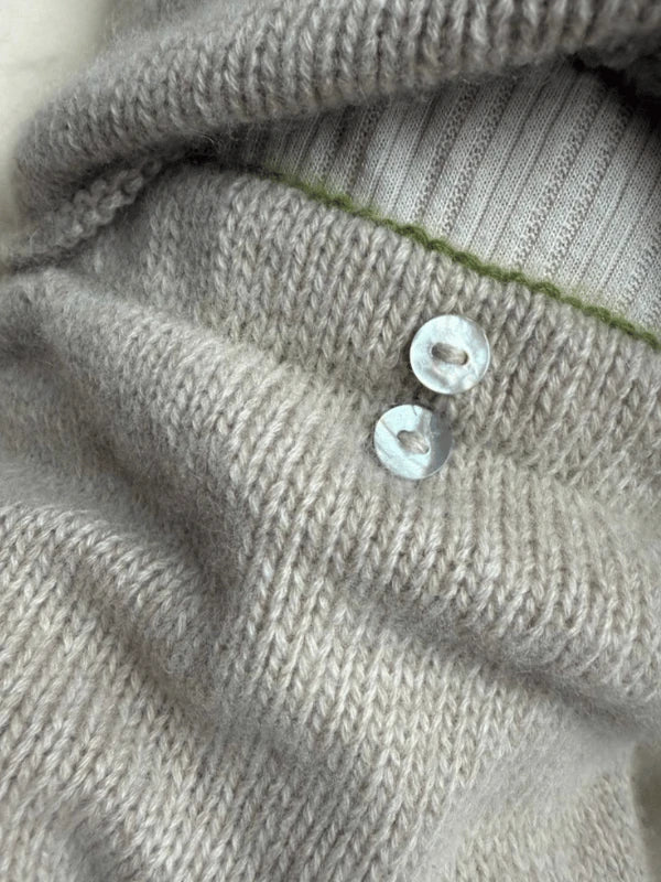 Close-up of soft, light gray knit fabric from the Petiteknit Cleo Baby Set neuleohje Suomi, featuring two translucent buttons and ribbed white and green material underneath. Detailed textures offer inspiring ideas for vauvan neuleet.