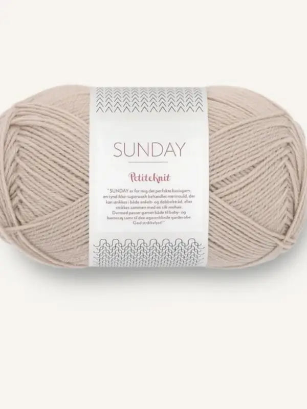 A skein of beige mulesing-free merino wool yarn labeled Sandnes Garn Sunday on a white background, with decorative text and patterns on the label.