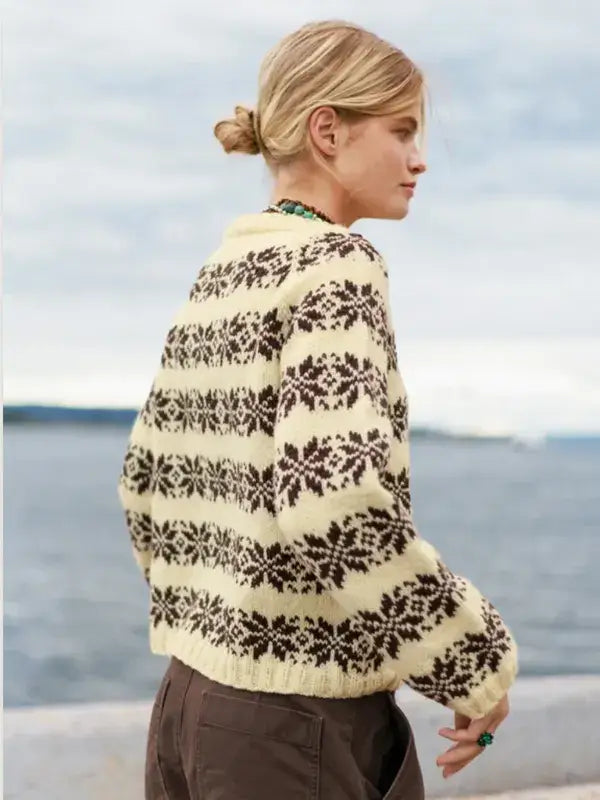 A person wearing a cream-colored Sandnes Garn Alvar – neulesetti Atlas featuring a dark brown floral-inspired fair isle pattern.
