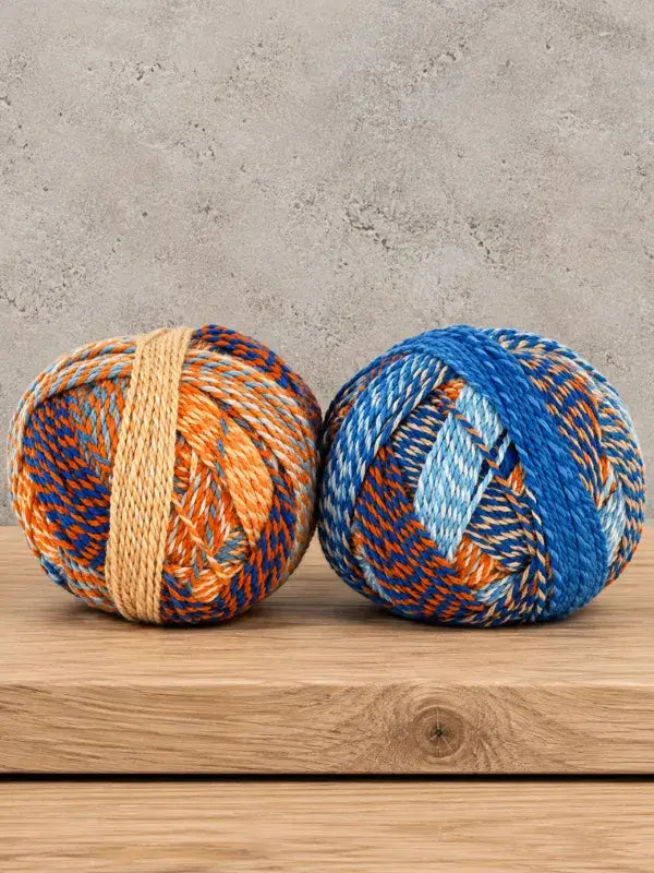 Two balls of Schoppel-Wolle Edition 3 variegated yarn in shades of blue and orange sitting on a wooden surface.