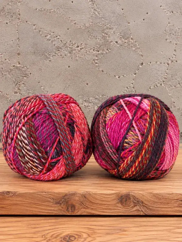 Two balls of Schoppel-Wolle Edition 3 variegated yarn in shades of pink, red, and dark purple.