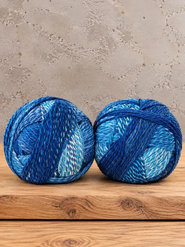 Two Schoppel-Wolle Edition 3 yarn balls in shades of blue and white, sitting side-by-side on a wooden surface.