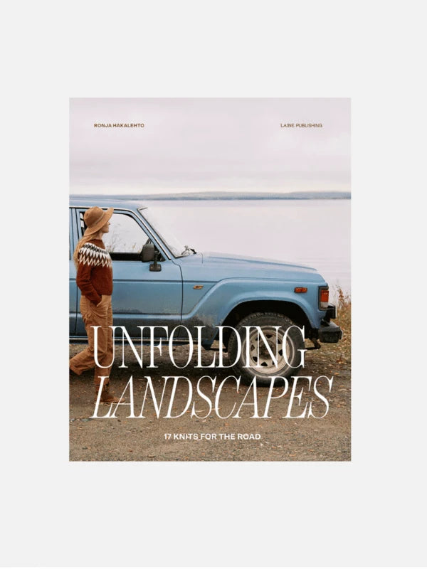 A person in a hat and patterned sweater stands beside a blue SUV by a lake in Northern Finland, featuring Ronja Hakalehto Unfolding Landscapes – 17 Knits for the Road ENG, an inspiring knitwear collection.