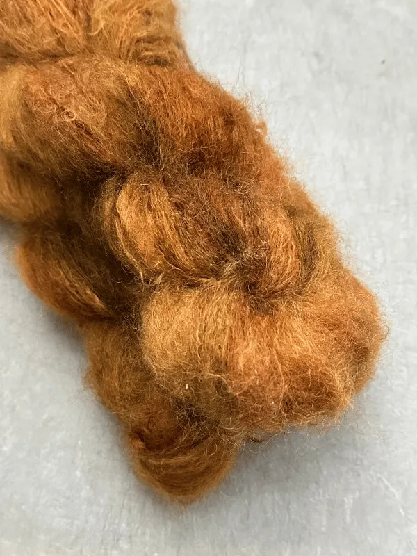 A close-up of soft, reddish-brown fluffy fiber on a light gray surface—perfect for your next Rhuska pipo neuleohje + WoolWomen Fluff Mohair project.