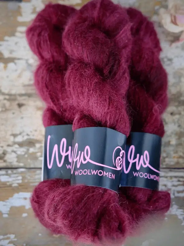 Two skeins of deep burgundy WoolWomen Silk Mohair yarn rest on a weathered wooden surface, showcasing the luxurious softness of this käsinvärjätty silkki-mohairlanka—perfect for your next elegant knitting project.