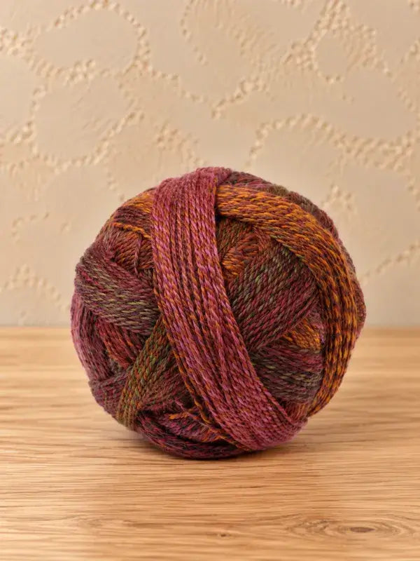 A ball of Schoppel wolle Zauberball crazy yarn in blended shades of purple, orange, and green.