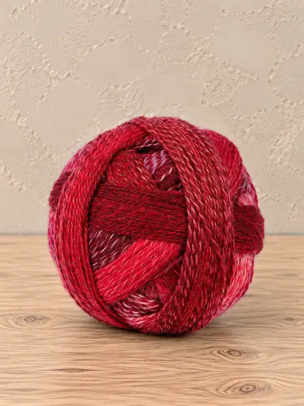 A round ball of Schoppel wolle Zauberball crazy yarn in variegated shades of red, ranging from deep crimson to bright pink and white.