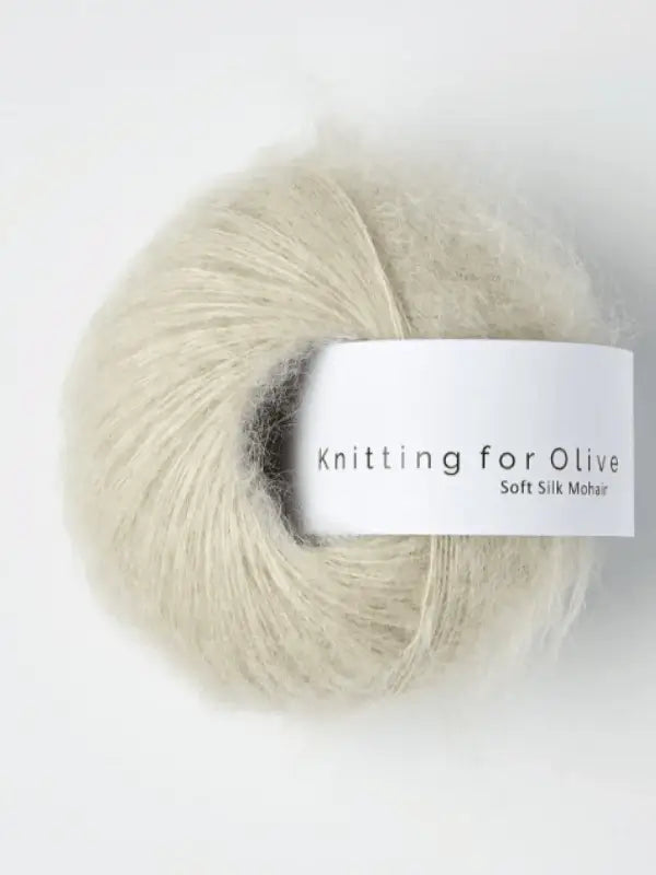 A ball of pale, fluffy yarn labeled Knitting for Olive Soft Silk Mohair rests on a white surface. This luxurious kid mohair yarn is crafted in accordance with the Responsible Mohair Standard.