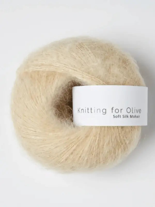 A ball of soft, light beige "Knitting for Olive Soft Silk Mohair" yarn with a white paper band wrapped around the middle, featuring high-quality Kid mohair certified by the Responsible Mohair Standard.