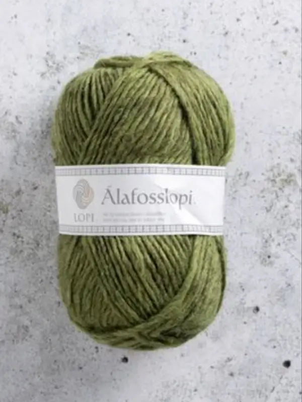 A skein of green Istex Alafosslopi yarn, made from islantilainen villa, lies on a lightly speckled gray surface.