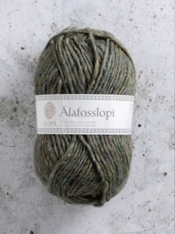 A skein of Istex Alafosslopi in greyish-green rests on a light, speckled concrete surface.