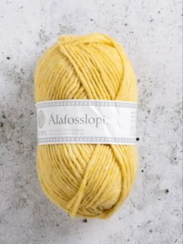 A skein of yellow yarn labeled Istex Alafosslopi, an icelandic wool yarn renowned for its warmth and durability, rests on a light gray, textured surface.