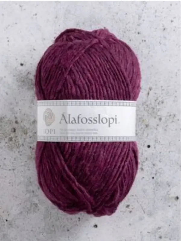 A skein of deep purple Istex Alafosslopi, a renowned islantilainen villalanka, with a white label rests on a light gray, speckled surface.