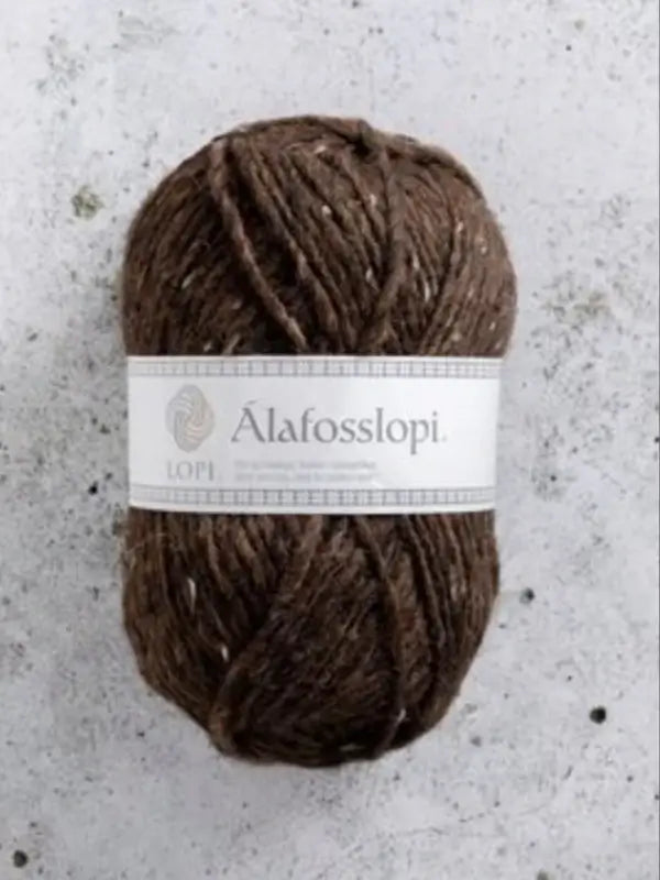 A ball of brown Istex Alafosslopi yarn with a white label rests on a light gray, speckled surface.